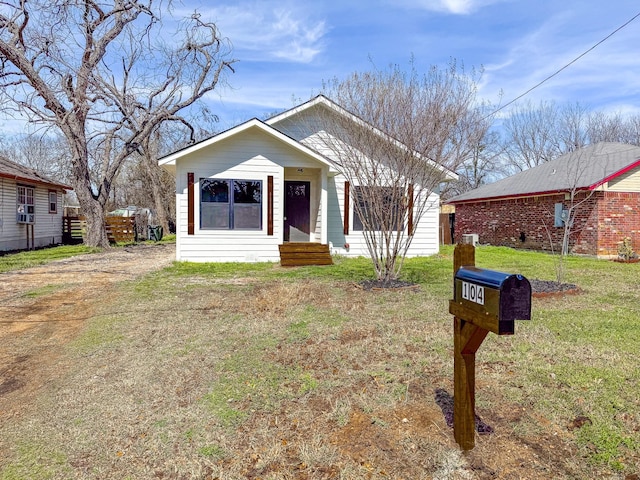 bungalow with cooling unit, a front yard, and dirt driveway