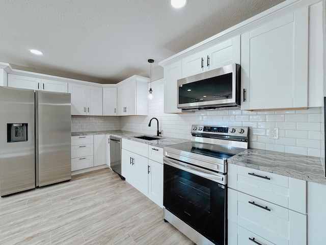 kitchen featuring light stone countertops, a sink, white cabinets, appliances with stainless steel finishes, and tasteful backsplash