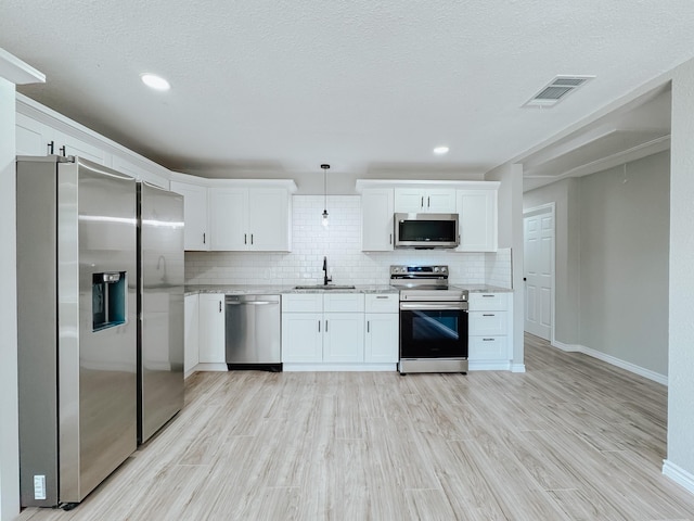 kitchen with visible vents, a sink, tasteful backsplash, light wood-style floors, and appliances with stainless steel finishes