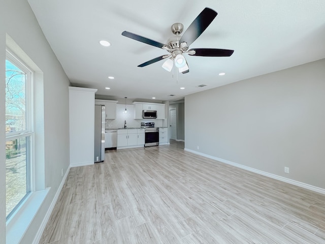 unfurnished living room with visible vents, a sink, recessed lighting, light wood finished floors, and baseboards