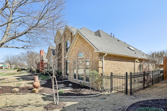 view of home's exterior featuring brick siding, a shingled roof, and fence