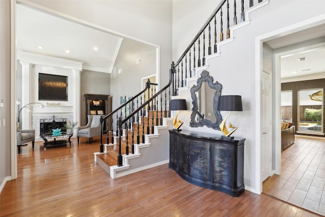 staircase with a towering ceiling, a fireplace, baseboards, and wood finished floors