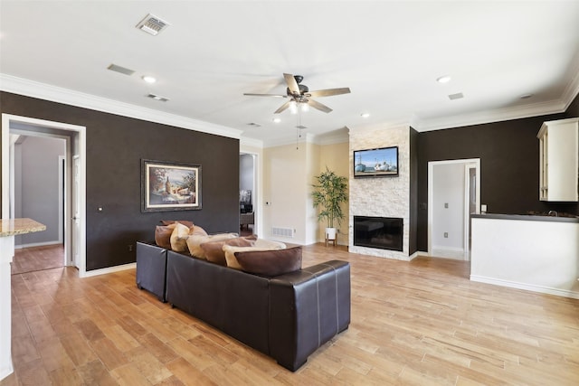 living area featuring visible vents, light wood-style flooring, a fireplace, and ornamental molding