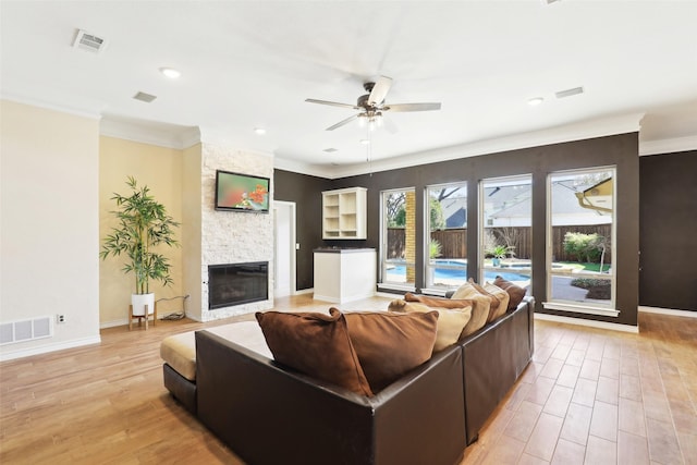 living area with visible vents, light wood-style flooring, a stone fireplace, and ceiling fan