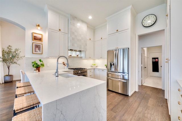 kitchen with a breakfast bar area, appliances with stainless steel finishes, a peninsula, wood finished floors, and a sink