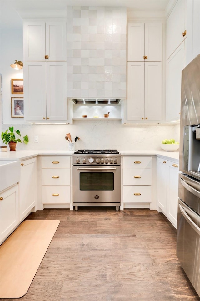 kitchen featuring wall chimney range hood, white cabinetry, appliances with stainless steel finishes, and light countertops