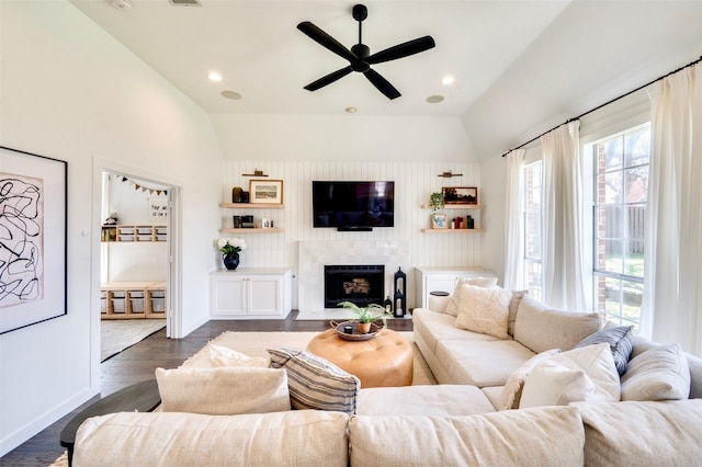 living area with a fireplace with raised hearth, vaulted ceiling, recessed lighting, a ceiling fan, and dark wood-style flooring