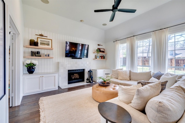 living area with dark wood finished floors, plenty of natural light, a fireplace, and ceiling fan