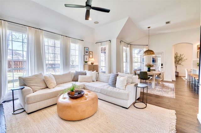 living room featuring a ceiling fan, wood finished floors, visible vents, baseboards, and arched walkways