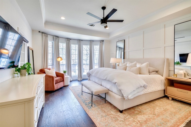 bedroom with visible vents, ceiling fan, light wood-style flooring, a decorative wall, and a raised ceiling