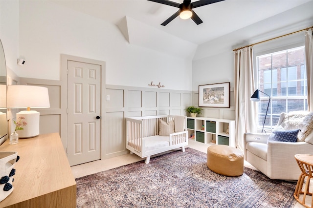 sitting room with a ceiling fan, a decorative wall, carpet flooring, wainscoting, and vaulted ceiling