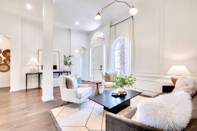 living area featuring wood finished floors, arched walkways, crown molding, a decorative wall, and baseboards