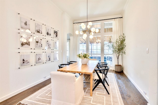 dining space featuring wood finished floors, baseboards, arched walkways, ornamental molding, and a notable chandelier