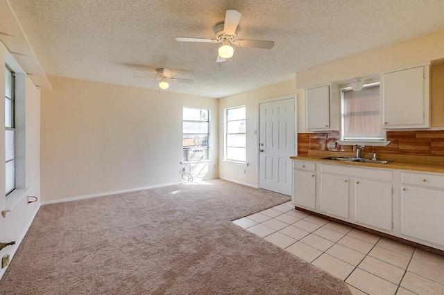 kitchen featuring light carpet, decorative backsplash, white cabinetry, and a sink