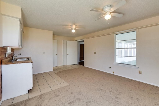 kitchen featuring light tile patterned flooring, a sink, white cabinets, a textured ceiling, and light carpet