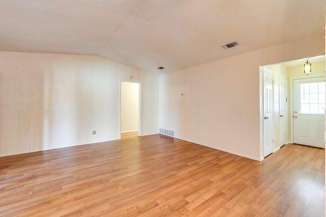 unfurnished room with visible vents, a textured ceiling, lofted ceiling, and light wood-style floors