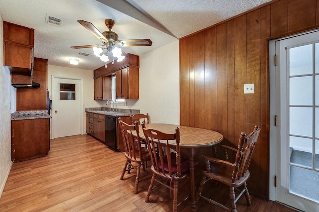 dining room featuring light wood finished floors, visible vents, ceiling fan, wood walls, and a textured ceiling