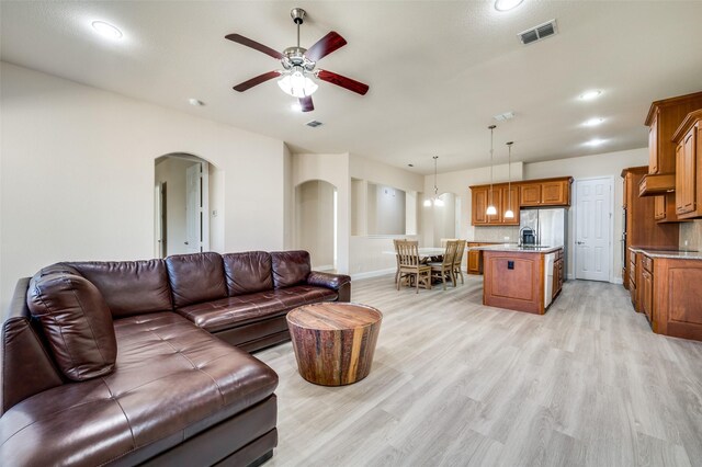 living room with arched walkways, visible vents, light wood-style flooring, and a ceiling fan