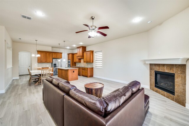 living room featuring visible vents, light wood-style flooring, a ceiling fan, baseboards, and a tile fireplace