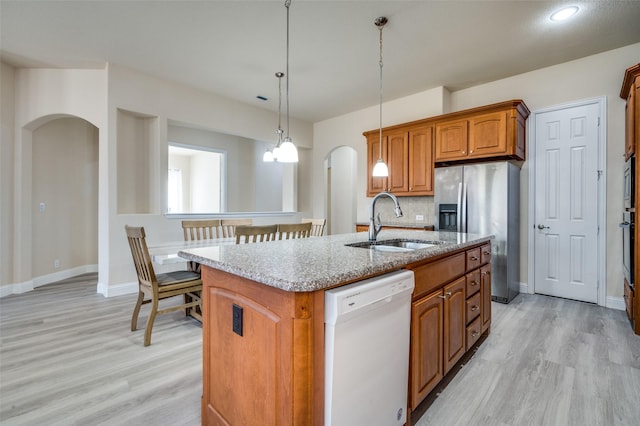 kitchen featuring a kitchen island with sink, arched walkways, a sink, dishwasher, and stainless steel fridge