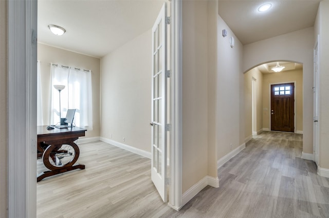 hall featuring light wood-style flooring, baseboards, and arched walkways