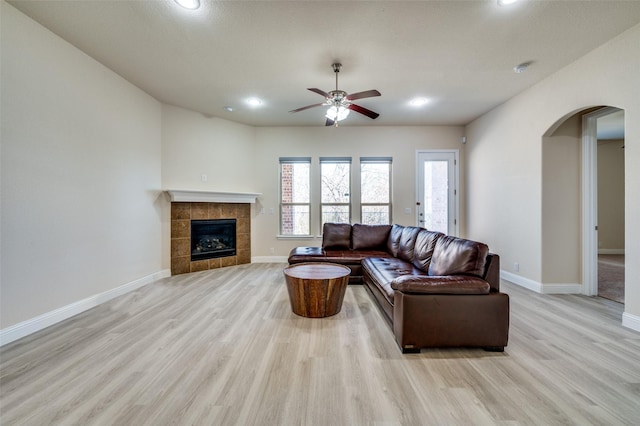 living area with a tiled fireplace, light wood-style floors, arched walkways, and baseboards