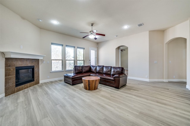 living area with a tile fireplace, visible vents, arched walkways, and light wood-type flooring