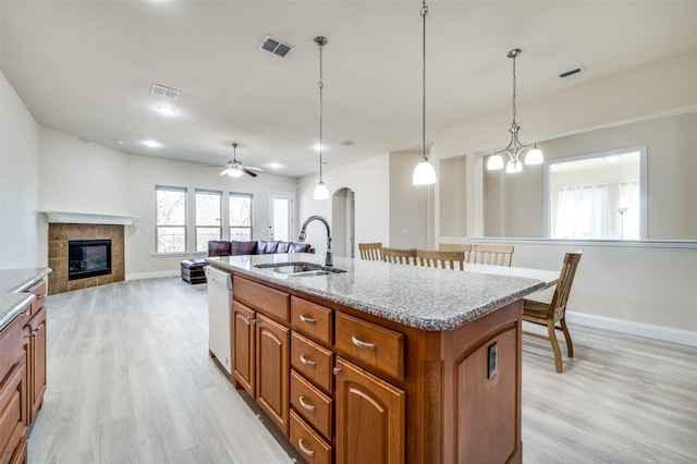 kitchen with brown cabinetry, visible vents, a fireplace, a sink, and light wood-style floors