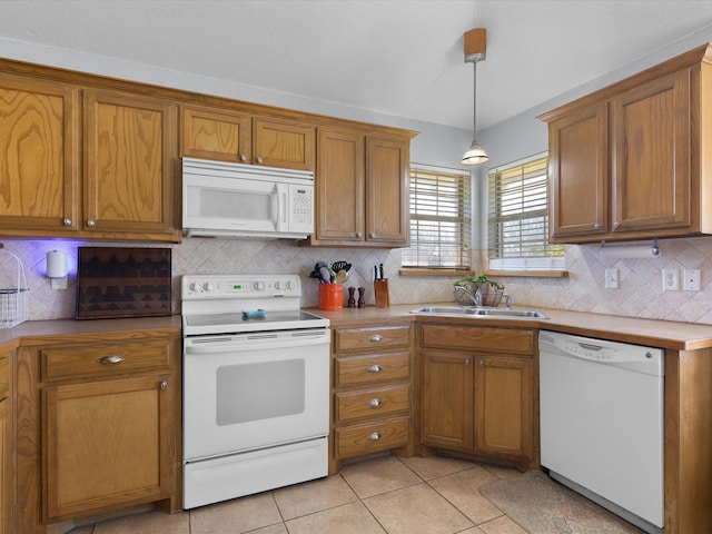 kitchen with a sink, tasteful backsplash, white appliances, light tile patterned flooring, and brown cabinetry