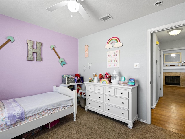 bedroom with visible vents, ceiling fan, dark carpet, a fireplace, and a textured ceiling