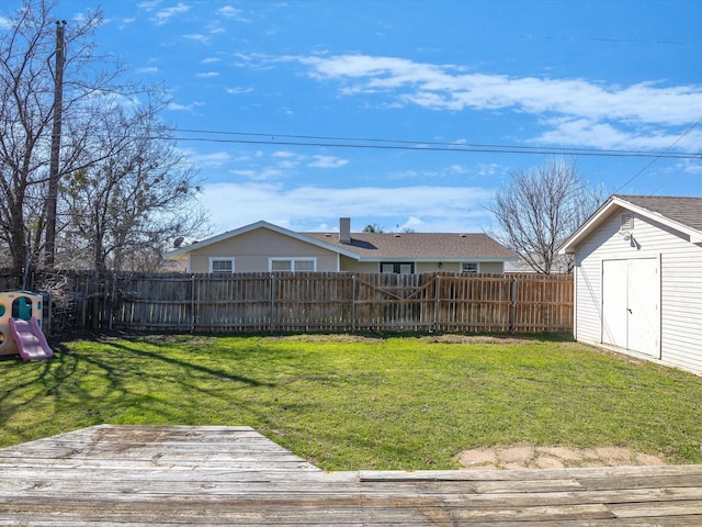 view of yard featuring a wooden deck, a fenced backyard, an outdoor structure, a storage unit, and a playground