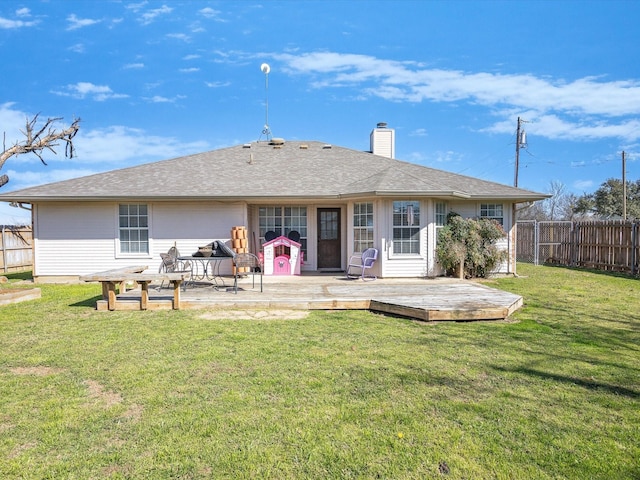 back of property featuring fence, a wooden deck, roof with shingles, a chimney, and a yard