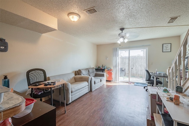 living room with a textured ceiling, wood finished floors, visible vents, and ceiling fan