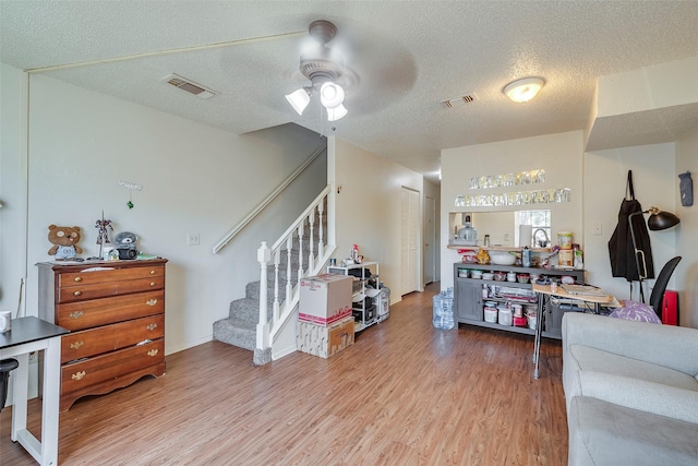 living area with visible vents, stairway, ceiling fan, and wood finished floors