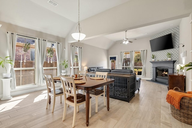 dining room featuring lofted ceiling, light wood-style floors, visible vents, and a large fireplace