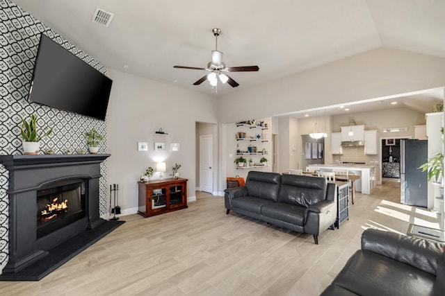 living room with a glass covered fireplace, lofted ceiling, light wood-style flooring, and visible vents