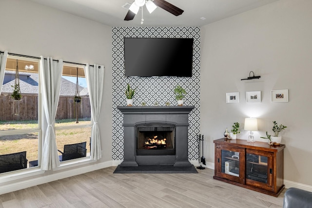 living area with a ceiling fan, light wood-style floors, baseboards, and a large fireplace