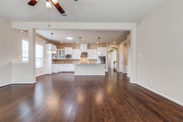 unfurnished living room with visible vents, a ceiling fan, dark wood finished floors, arched walkways, and baseboards