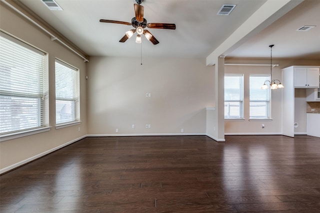 unfurnished living room featuring a wealth of natural light, visible vents, dark wood-type flooring, and ceiling fan with notable chandelier