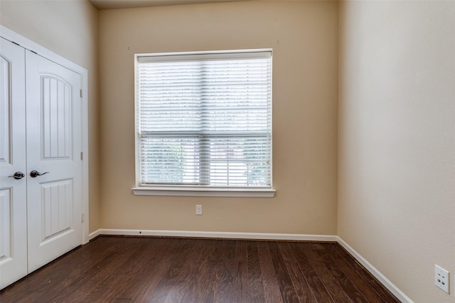 spare room with baseboards and dark wood-style flooring