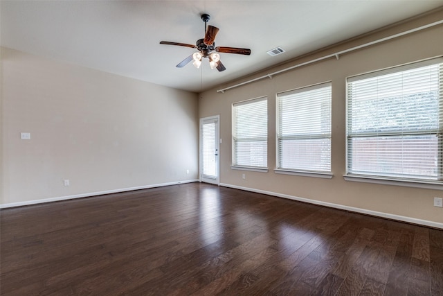 empty room featuring dark wood finished floors, a ceiling fan, visible vents, and baseboards