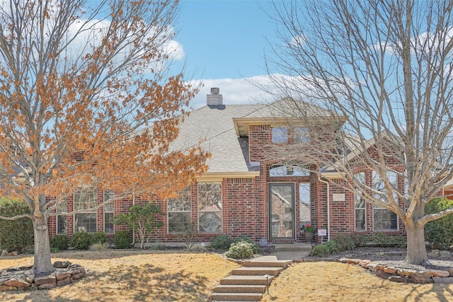 view of front of house featuring brick siding, a chimney, and a shingled roof