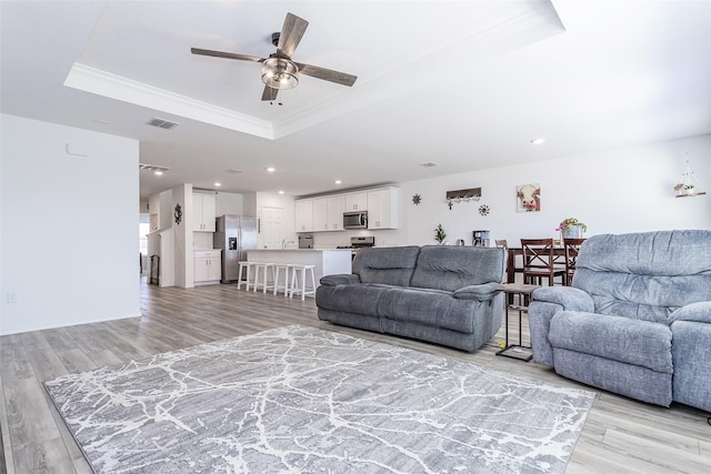 living area with a raised ceiling, recessed lighting, light wood-style floors, and visible vents