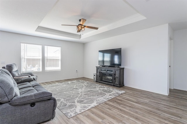 living area featuring crown molding, baseboards, ceiling fan, wood finished floors, and a raised ceiling