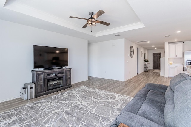 living room with light wood finished floors, visible vents, a raised ceiling, and ceiling fan