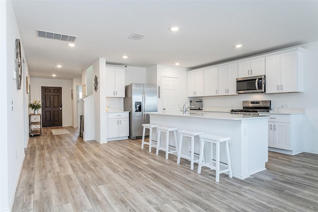 kitchen with light wood-type flooring, stainless steel appliances, a kitchen breakfast bar, and visible vents