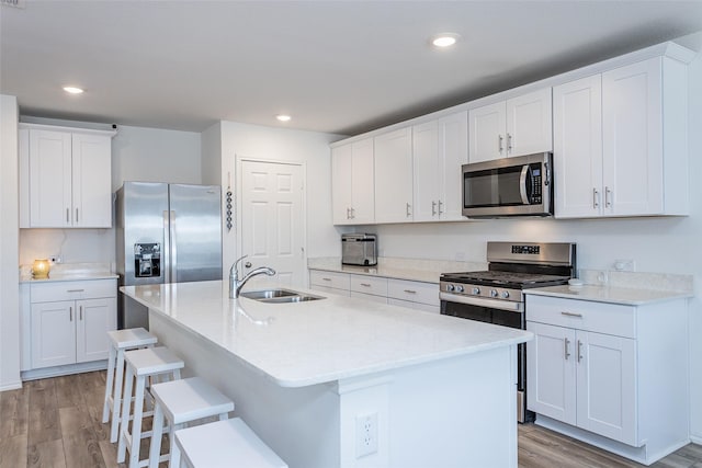 kitchen with a kitchen island with sink, light wood-style flooring, appliances with stainless steel finishes, and a sink