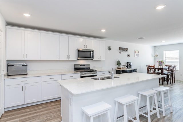 kitchen with white cabinetry, stainless steel appliances, light wood-style floors, and a sink