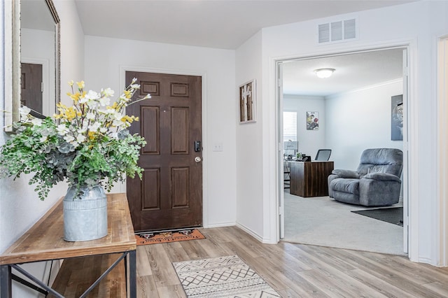 foyer featuring light wood finished floors, visible vents, crown molding, and baseboards