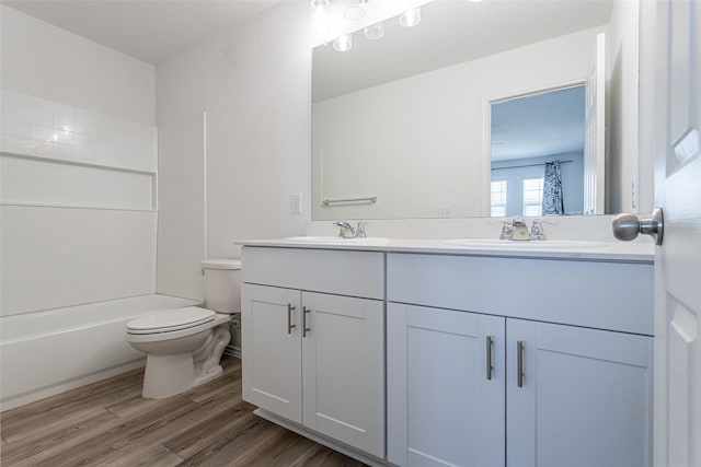 full bath with double vanity, toilet, wood finished floors, and a sink